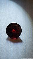 Photo of round faceted vivid red almandine garnet gemstone showing rich deep red color under direct light.