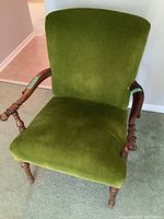 Front view of the green upholstered arm chair showing seat, backrest, and wooden arm details.