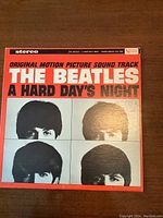 Front cover of the vinyl record album 'The Beatles A Hard Day's Night' original motion picture soundtrack showing red and white design with black and white headshots of the band members.