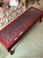 Top-down angled view of coffee table showing carved wooden inset beneath glass top and one carved leg.
