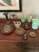 Wide view of all decorative items including jadeite pieces, decorative plates, metal candle holders, flower frog, and decorative tin.