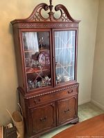 Front view of entire solid wood dining hutch with glass doors showing ornate carved crown and finial, two glass doors with lattice design, and lower drawers and cabinet.