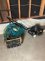 Photo showing Black & Decker electric lawn mower next to McCulloch hand push reel mower and coiled garden hose on cement floor.