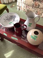 Large decorative bowl, smaller red pitcher, large beige pitcher, and round beige vase displayed on wooden coffee table.