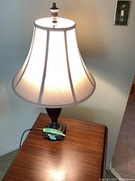 Large resin base table lamp illuminated on a wooden side table, showing fabric shade and overall design.