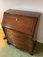 Front view of solid wood secretary desk with fold-down top closed, showing lock and brass handles.