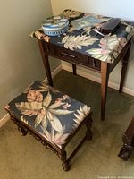 Matching wooden bench with floral fabric cushioned seat, turned legs and dark wood finish, alongside sewing machine stand.