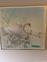Framed art print showing a swan with cygnets in water with reeds on left.