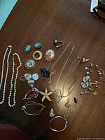 Full view of lot on wood table showing all costume jewelry items spread out including necklaces, brooches, bracelets, earrings and cufflinks.