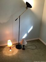 Four lamps displayed together: one tall black floor lamp, two small table lamps with white and red shades, and one small red body lamp with light fabric shade, showing overall condition and variety.