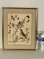Framed colored bird print photographed against a wall with a water bottle for scale; shows the entire artwork and frame.