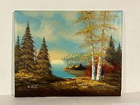 Full view of the signed landscape oil painting showing trees, lake, rocky shore, sky and artist's signature.