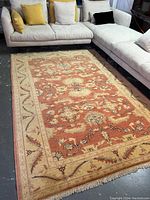 Full view of carpet laid in living area showing overall pattern, colors, border, and fringe.