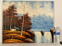 Full view of the landscape painting showing waterfall, trees, cabin, and sky with water bottle for scale.