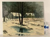 Full view of the oil painting showing the winter landscape with snow-covered ground, several trees, and two rustic buildings with snow on the roofs. Water bottle beside for scale.