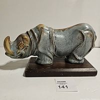 Side view of the Blue Mountain Pottery ceramic rhino figurine displaying the overall shape, colors, and the wood base.