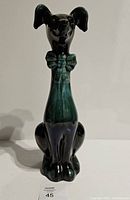 Front view of the tall long neck winking dog figurine showing the dark green and black glossy glaze and detailed bow on the neck.