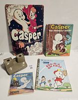 Photo showing all five Casper items as viewed from above on a white surface. Includes the tin sign, two books, a View-Master reel pack, and three View-Master viewers.