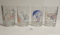 Four clear drinking glasses showing vintage Disney character illustrations including Donald Duck and Mickey Mouse in celebration scenes.