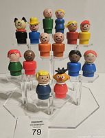 Photo showing 14 Fisher-Price Little People figures in various colors and types displayed on a clear tiered plastic stand.