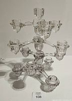 Clear glass tiered candle holder showing multiple arms and candle cups on three levels, photographed straight on with white background.