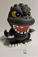 Front view of the Godzilla coin bank with detailed texture, big yellow eyes, and open mouth showing teeth.