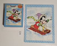 Photo showing completed Goofy puzzle with original box beside it. Puzzle features Goofy sledding in winter attire with a blue snowflake border.