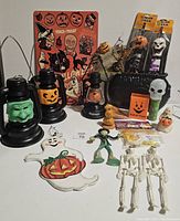 Photo showing varied small Halloween decorations including lanterns, figurines, a metal sign, and novelty items arranged on white surface.