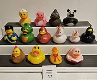 Front view of all 15 themed rubber ducks arranged in 3 rows on white risers, showcasing various animal and novelty themes including a panda, unicorn, ninja, dragon, and pixel art.