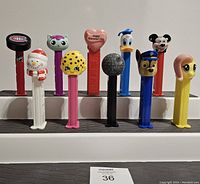 Front view of 10 Pez dispensers lined up showing various themed character heads and colorful sticks.