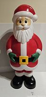 Santa Claus blow mold figure front view in natural light on beige background, detailed facial features and red/white/green/black color scheme.