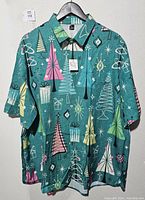 Front view of the retro Christmas tree themed shirt on hanger showing colorful trees and ornaments on teal background