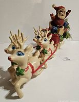 View of Santa Claus seated in red sleigh with two cream-colored reindeer in front, showing details of harness and reindeer faces with painted blue eyes and red noses.