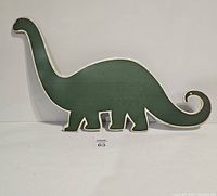 Tin metal sign shaped like a dinosaur, green on one side with white border.