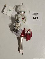 Full view of glass ornament lady wearing white furry jacket and hat, red dress, holding gifts and purse.