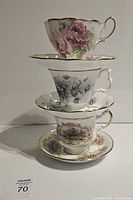 Side view of three stacked English tea cup sets showing floral designs and gold accents on cups and saucers.
