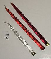 Three vintage lucite candles with two bright orange-red and one clear with silver flecks, laid flat on a surface with label 122 visible.