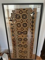 Full view of framed textile carpet measuring approximately 28 x 48 inches with tribal geometric patterns in shades of brown and black.