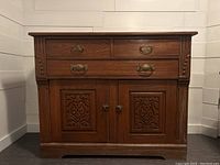 Front view of antique wooden dresser cupboard showing two drawers and two carved panel doors with brass handles