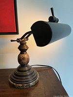 Front view of adjustable metal desk lamp on wood surface showing cylindrical black shade and round marble base