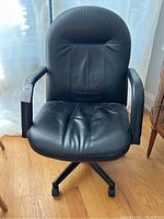 Front view showing the black leather seat and backrest, armrests, and chair base with casters.