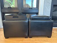 Front view of the two black leather storage boxes side by side, one with the cushioned top visible and the other with the tray placed on top.