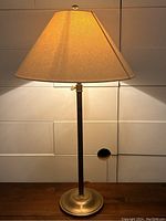 Brass table lamp illuminated showing cream conical shade and brass stand with round base.