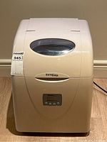 Front view of white Danby Ice'n Easy portable ice maker with label and digital control panel visible, placed on hardwood floor.