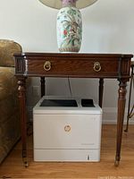 Side view of the French antique oak side table showing the turned legs with brass casters and brass ring handles on the drawer.