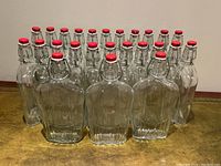 Front view of 24 clean clear glass bottles arranged in rows showing red lever style sealable lids