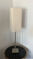 Full view of modern table lamp showing tall rectangular off-white fabric shade and brushed metal body with square base