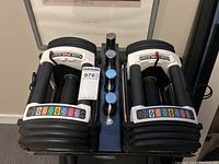 Pair of PowerBlock dumbbells on floor next to stand legs