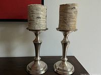 Front view of pair of silver plate candlesticks with birchbark pillar candles on top, showing design and condition.