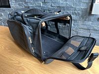 Side and front view of black Sherpa Original duffel style dog travel bag with front zippered mesh door open revealing padded interior and wooden rods.